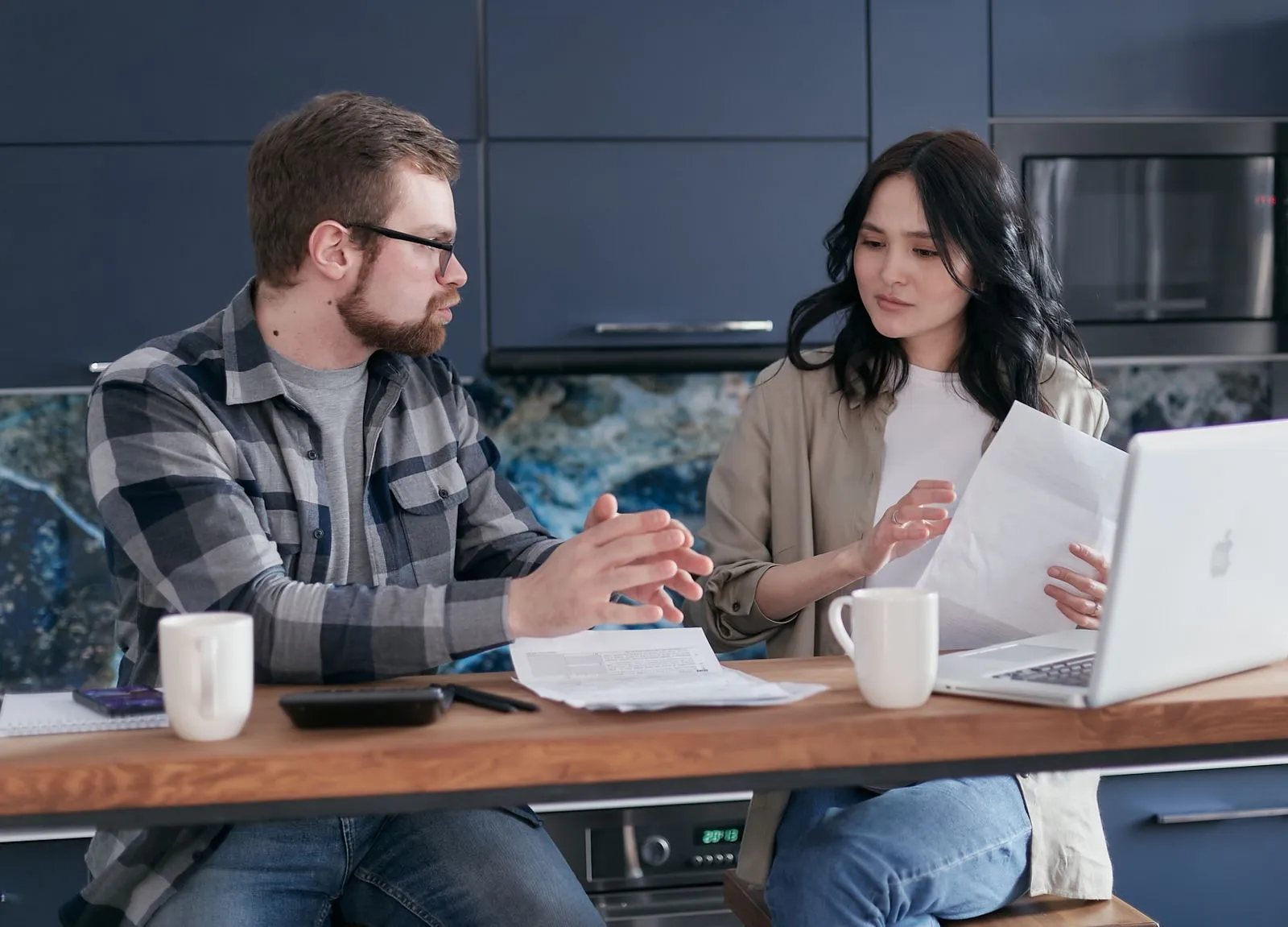 Young couple at a kitchen table with a laptop and paperwork reviewing bills