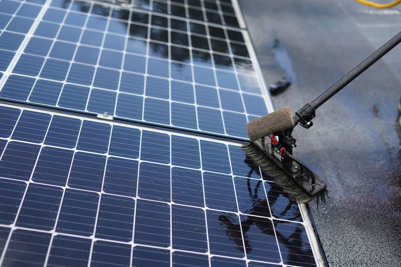 A wet rooftop solar panel being washed with a long-handled brush