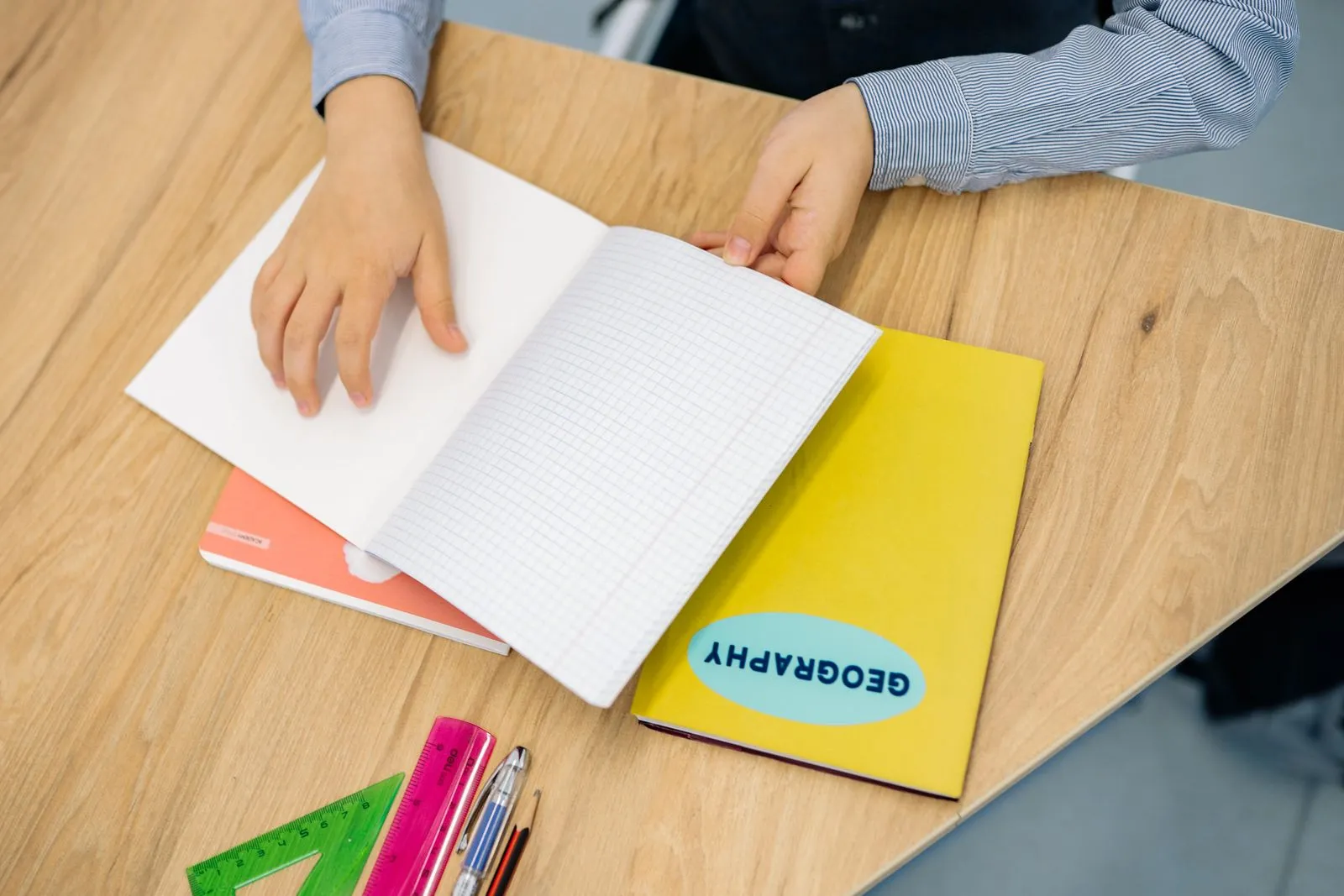 A child sitting at a wooden desk with an open notebook and pencils