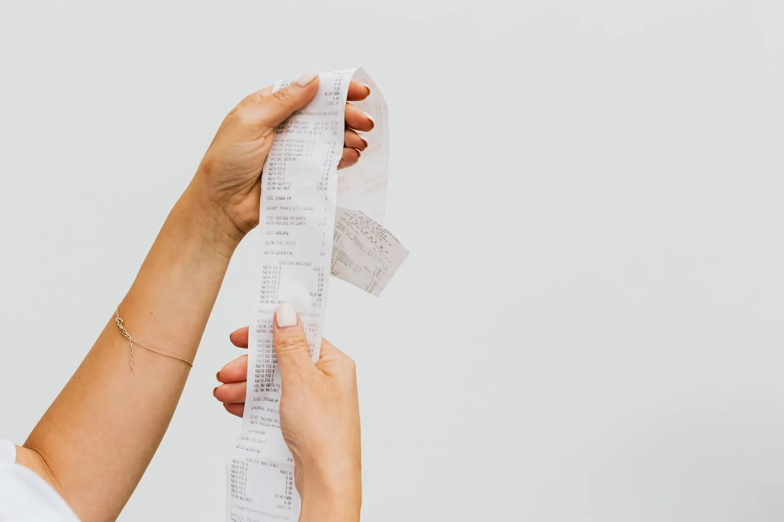 Person holding a grocery receipt beside a wallet on a kitchen counter