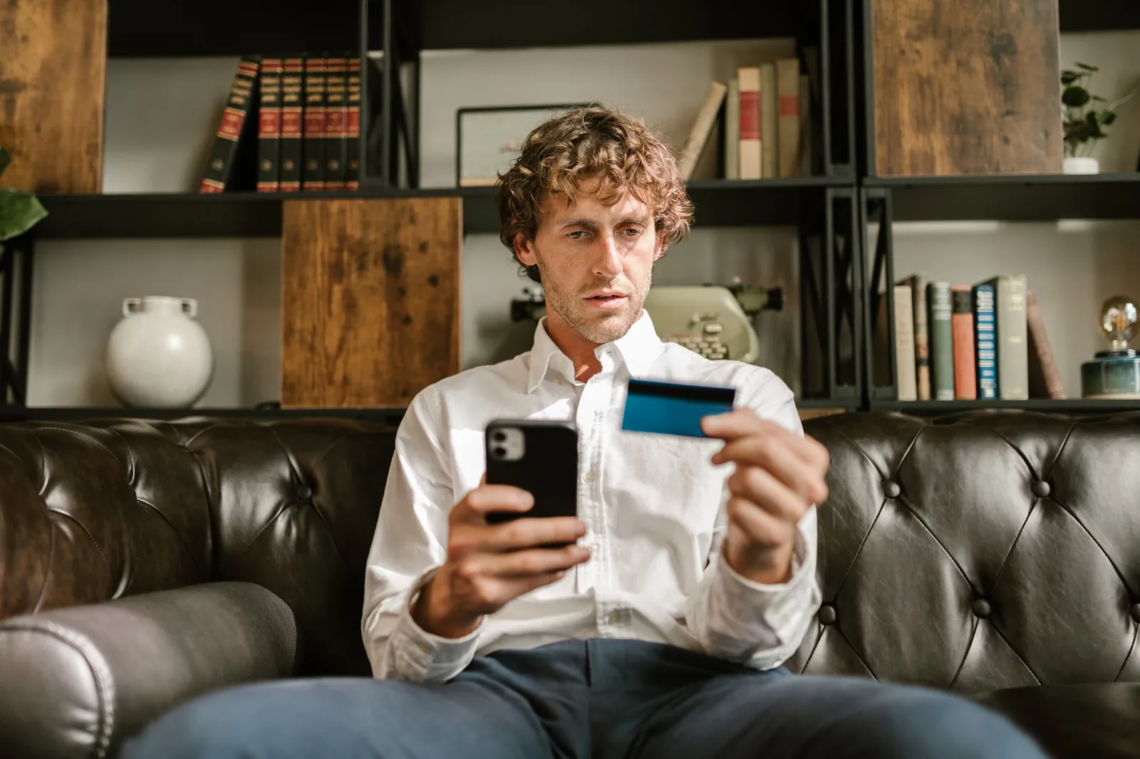 Person shopping online with a phone and credit card on a couch