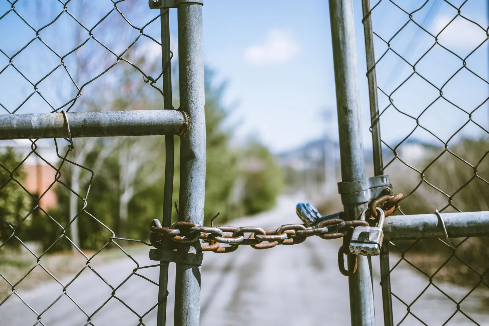 A rusty chain and padlock holding shut a chain-link gate across a dirt lane