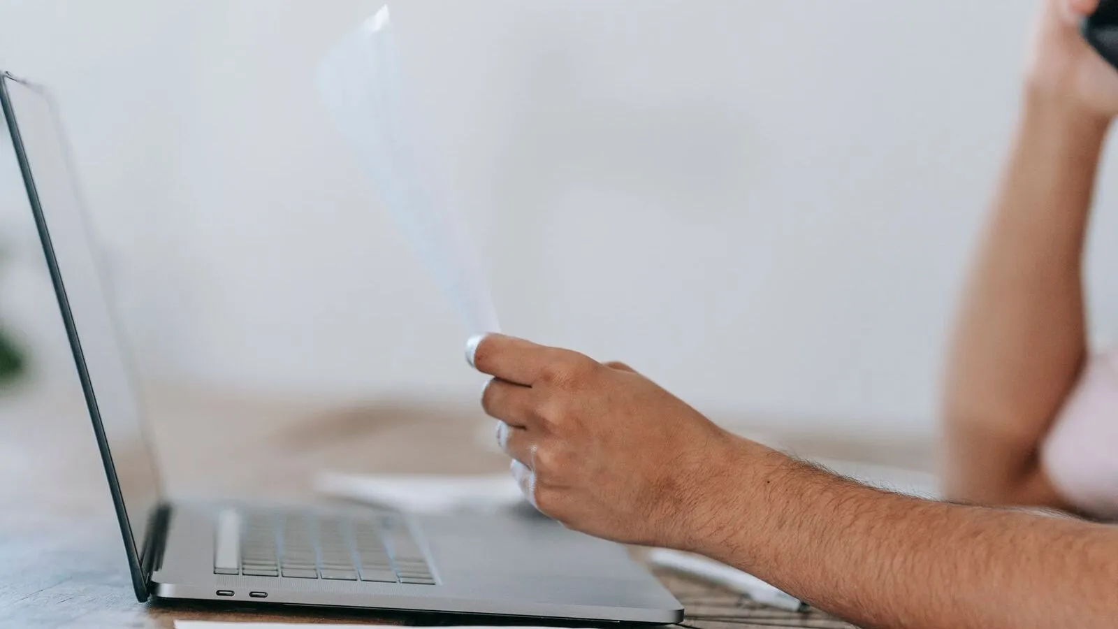 Person reading a paper credit report at a kitchen table with a laptop open
