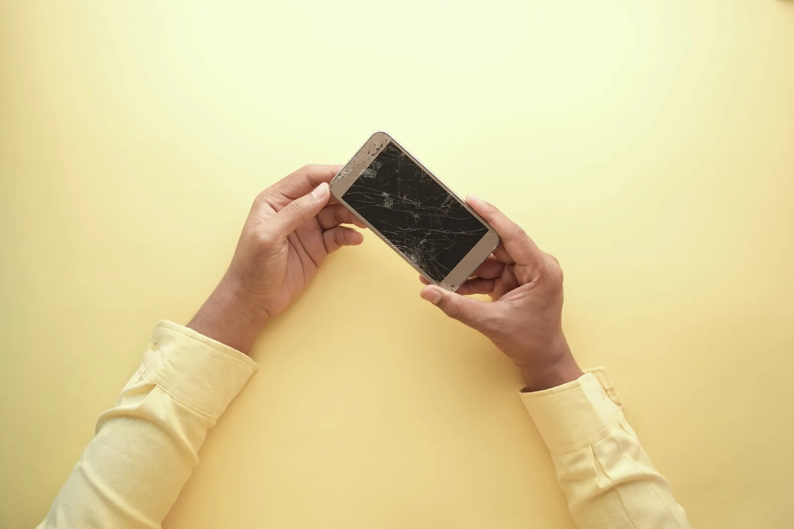 Person holding a smartphone with a cracked screen