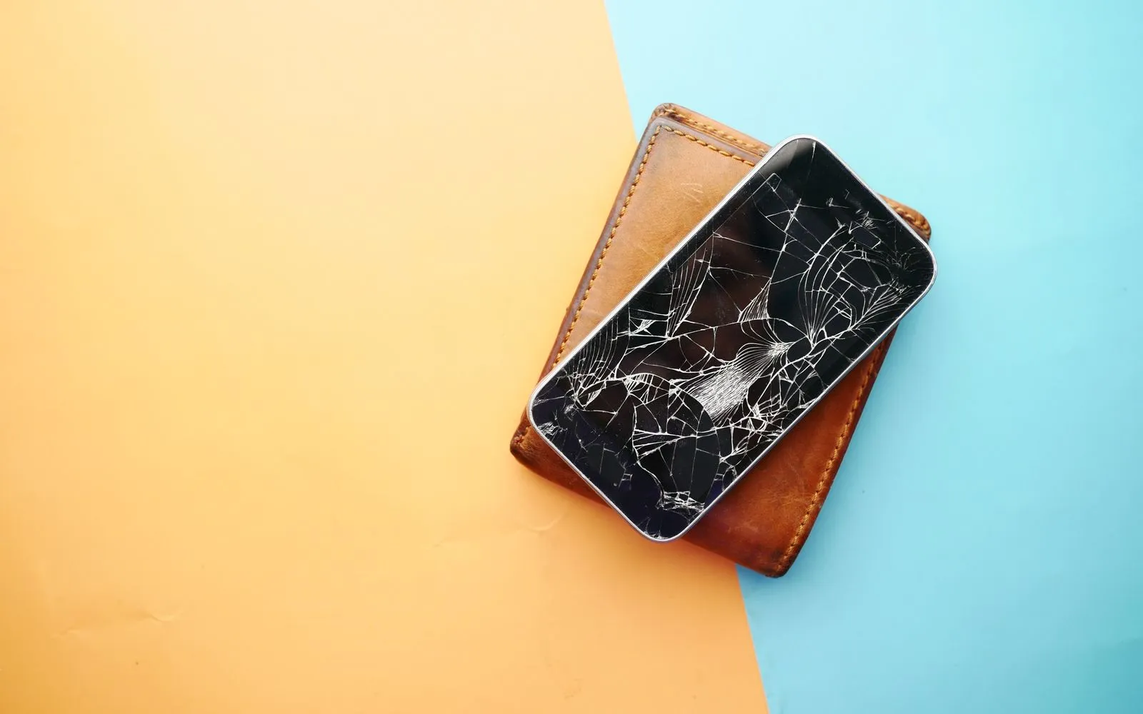 A person holding a cracked smartphone screen while sitting at a desk