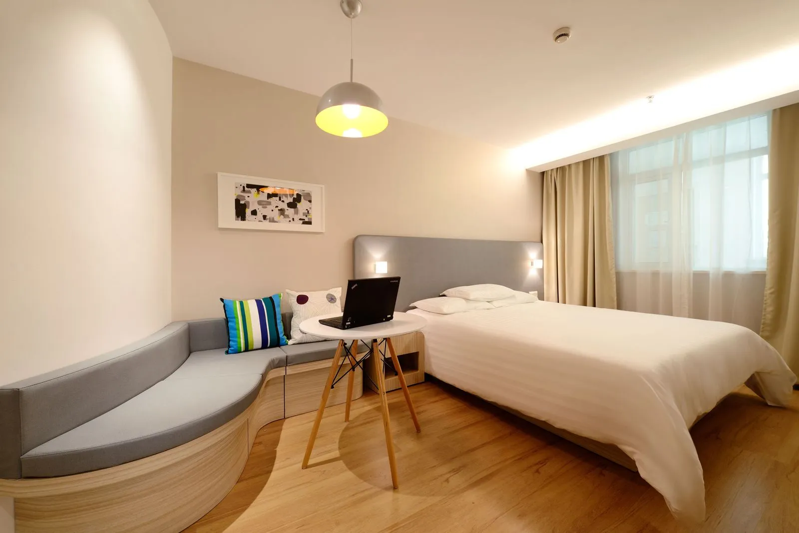 Modern hotel room with a made bed, laptop on the desk, and warm lamp lighting