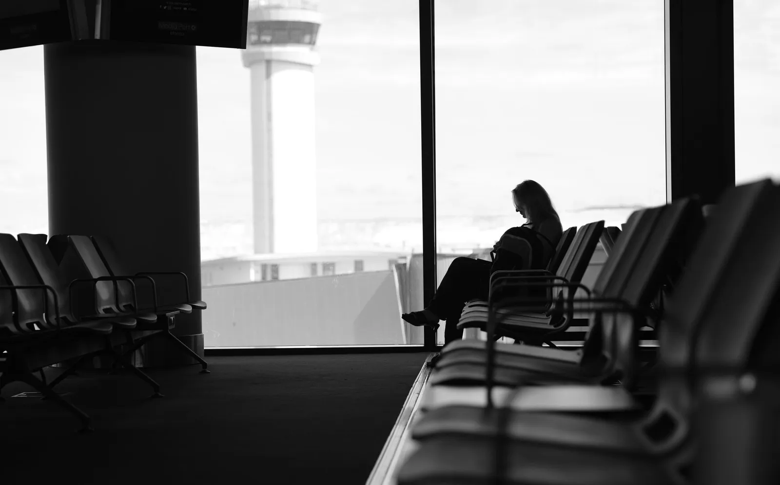 Traveler seated in an airport terminal lounge looking out toward the airfield