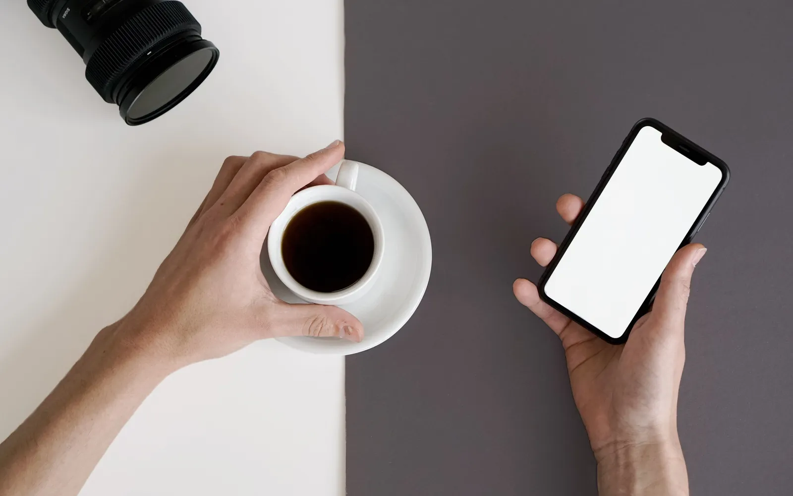 Hand holding a smartphone with a blank screen beside a cup of black coffee