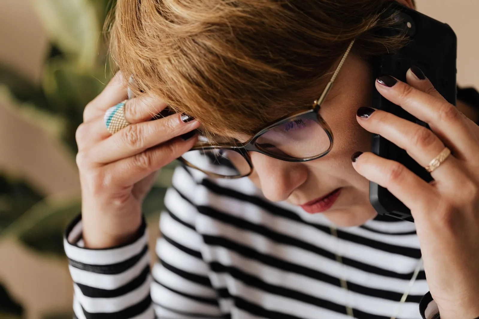 Woman in glasses holding a phone to her ear with a hand raised to her head
