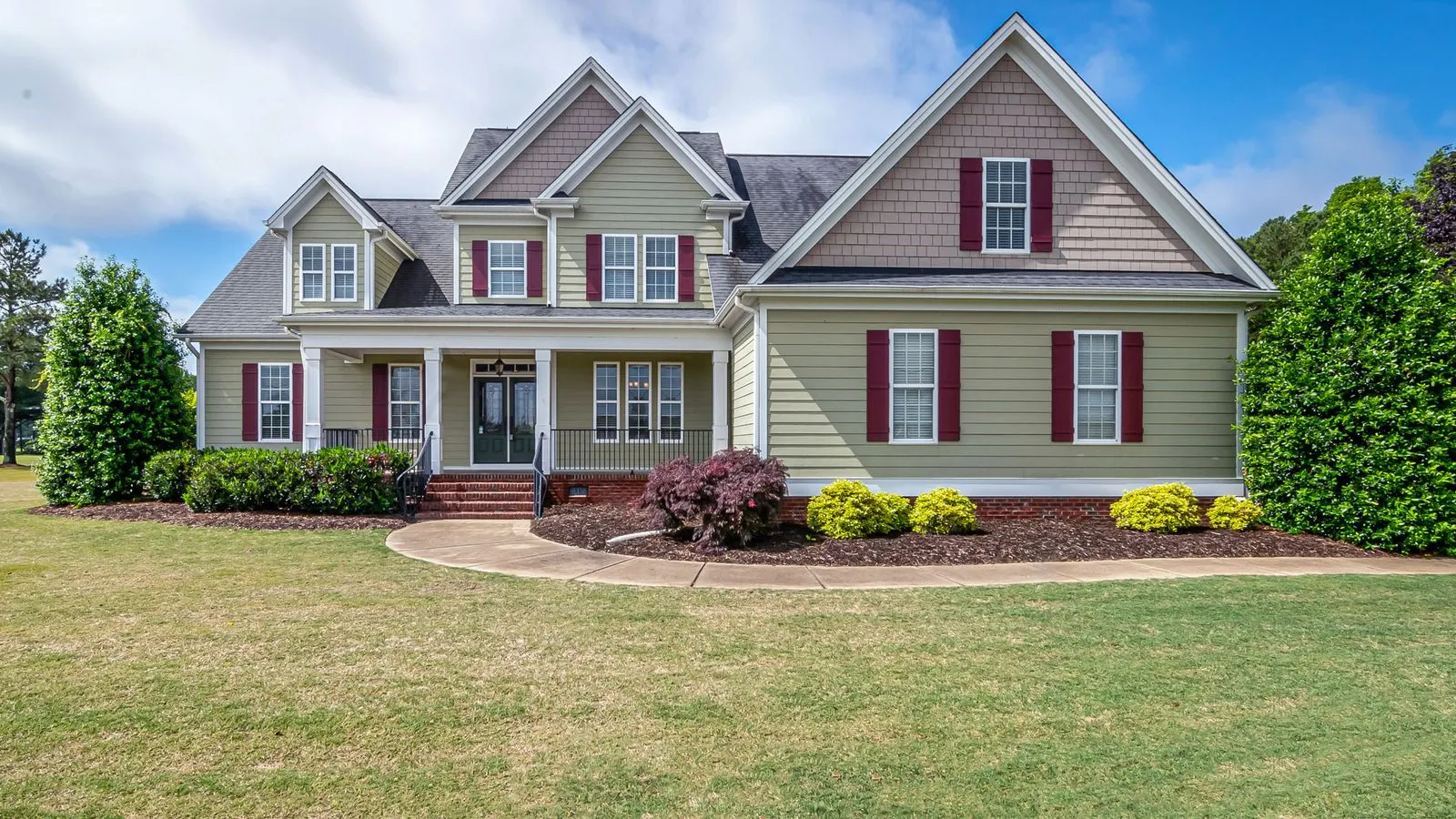 Two-story suburban house with red shutters, a front porch and a wide lawn