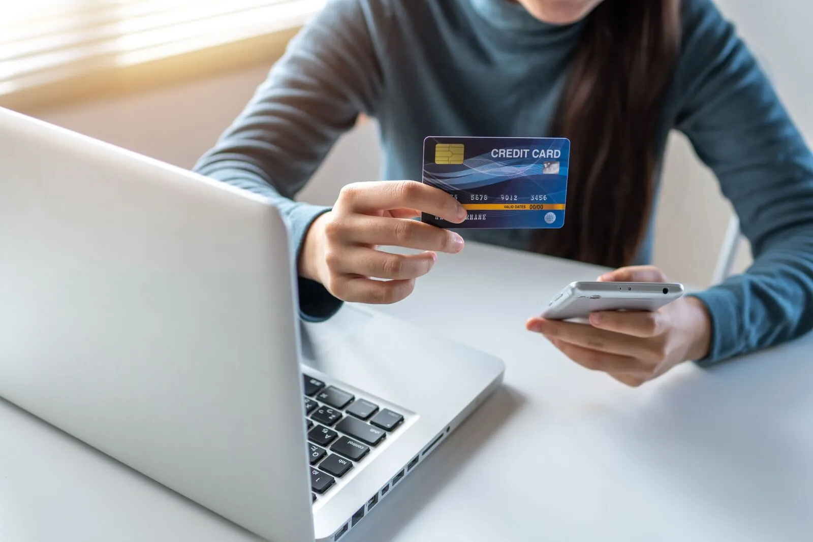 A person holding a credit card and using a mobile phone at a home desk