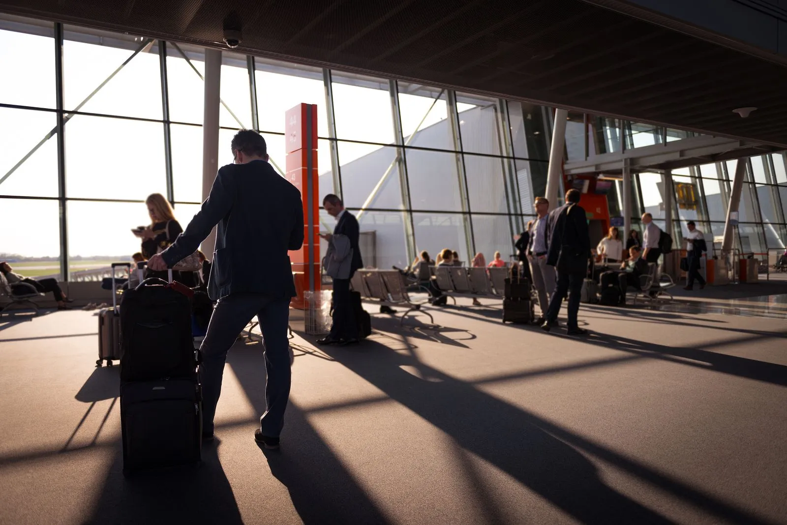 Travelers walking through a busy airport terminal with rolling luggage