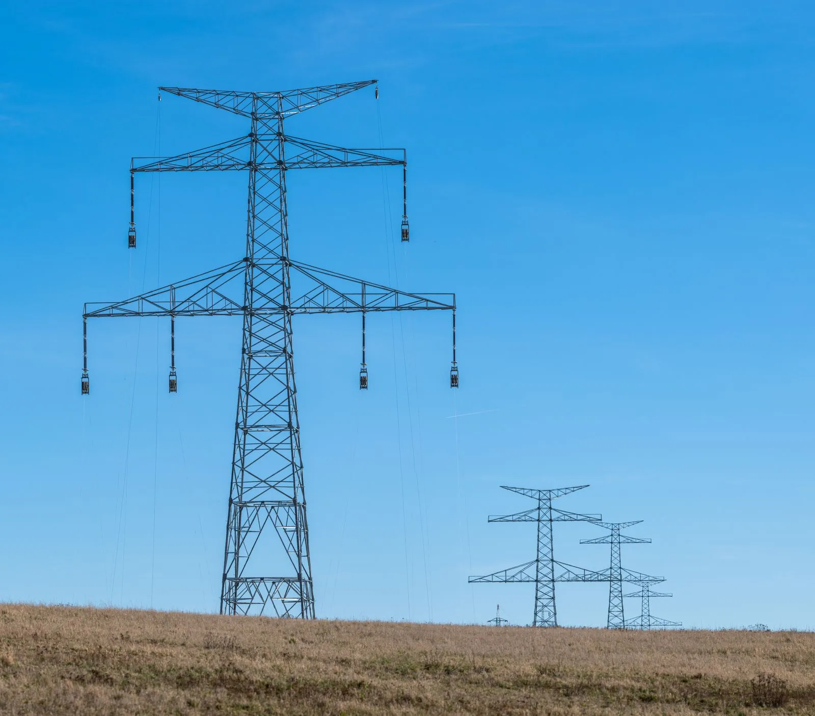 High-voltage transmission lines and towers running across open countryside at dusk