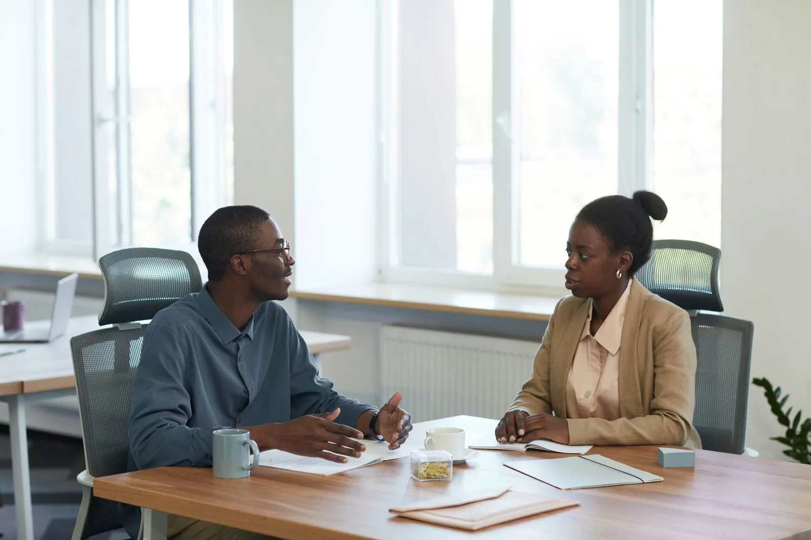 Two coworkers talking across a desk in a bright office