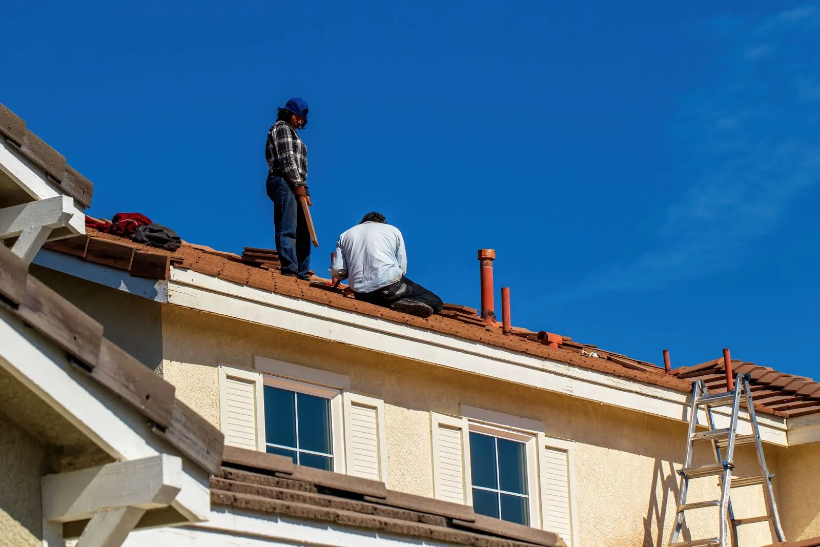 Workers on a tiled residential roof under a clear blue sky