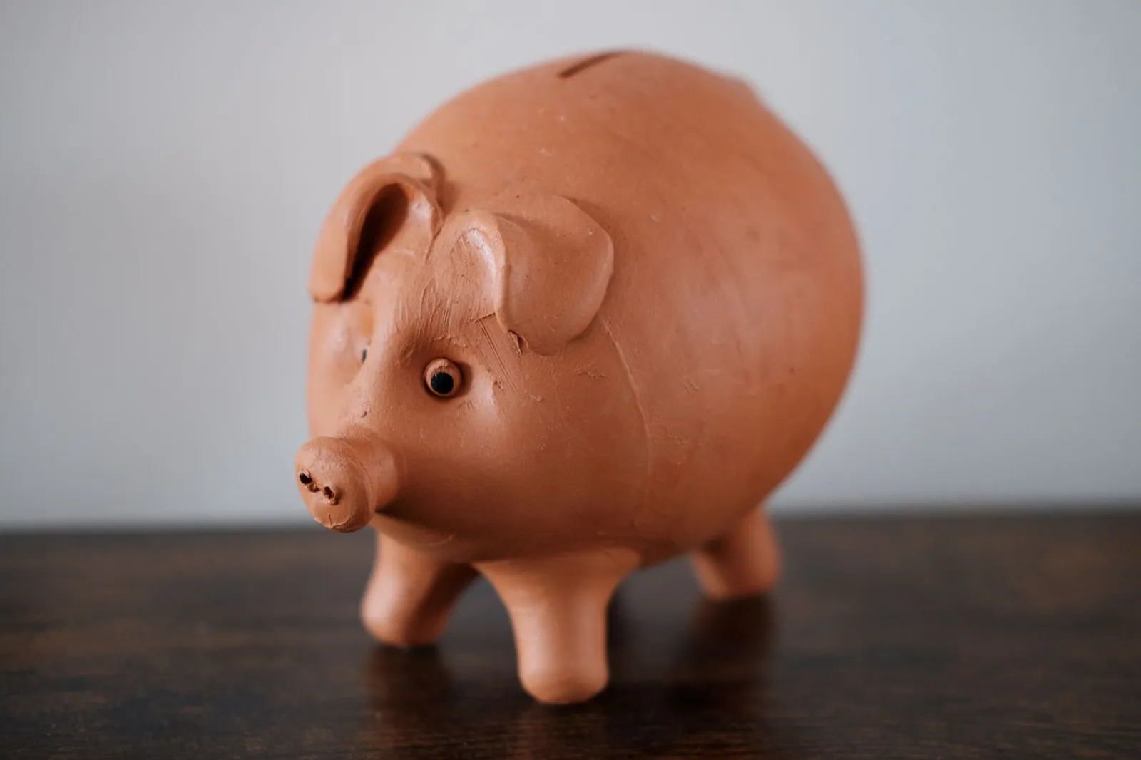 Terracotta piggy bank standing on a dark wooden tabletop against a plain wall