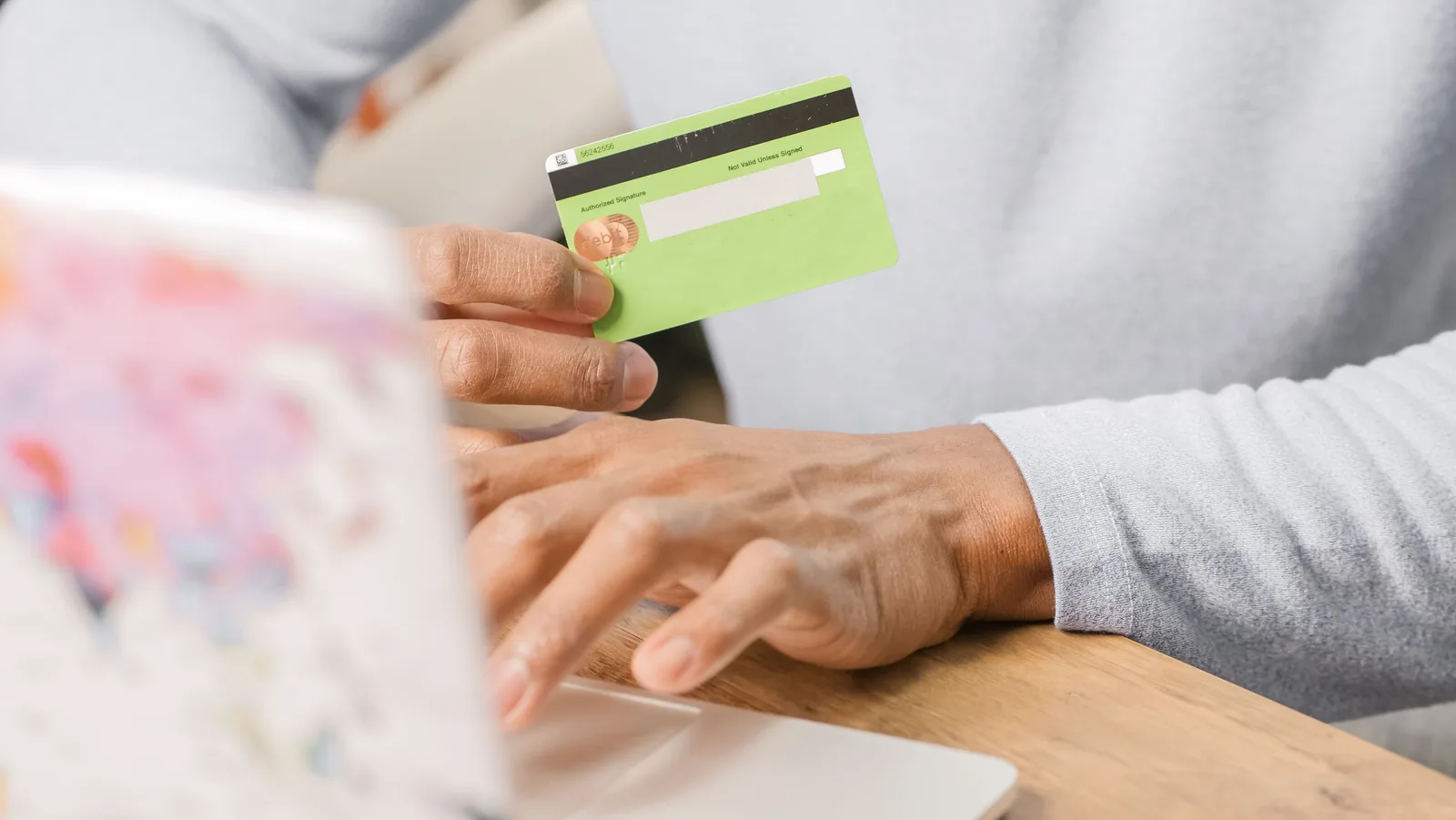 Person entering a credit card number into a laptop at a kitchen counter