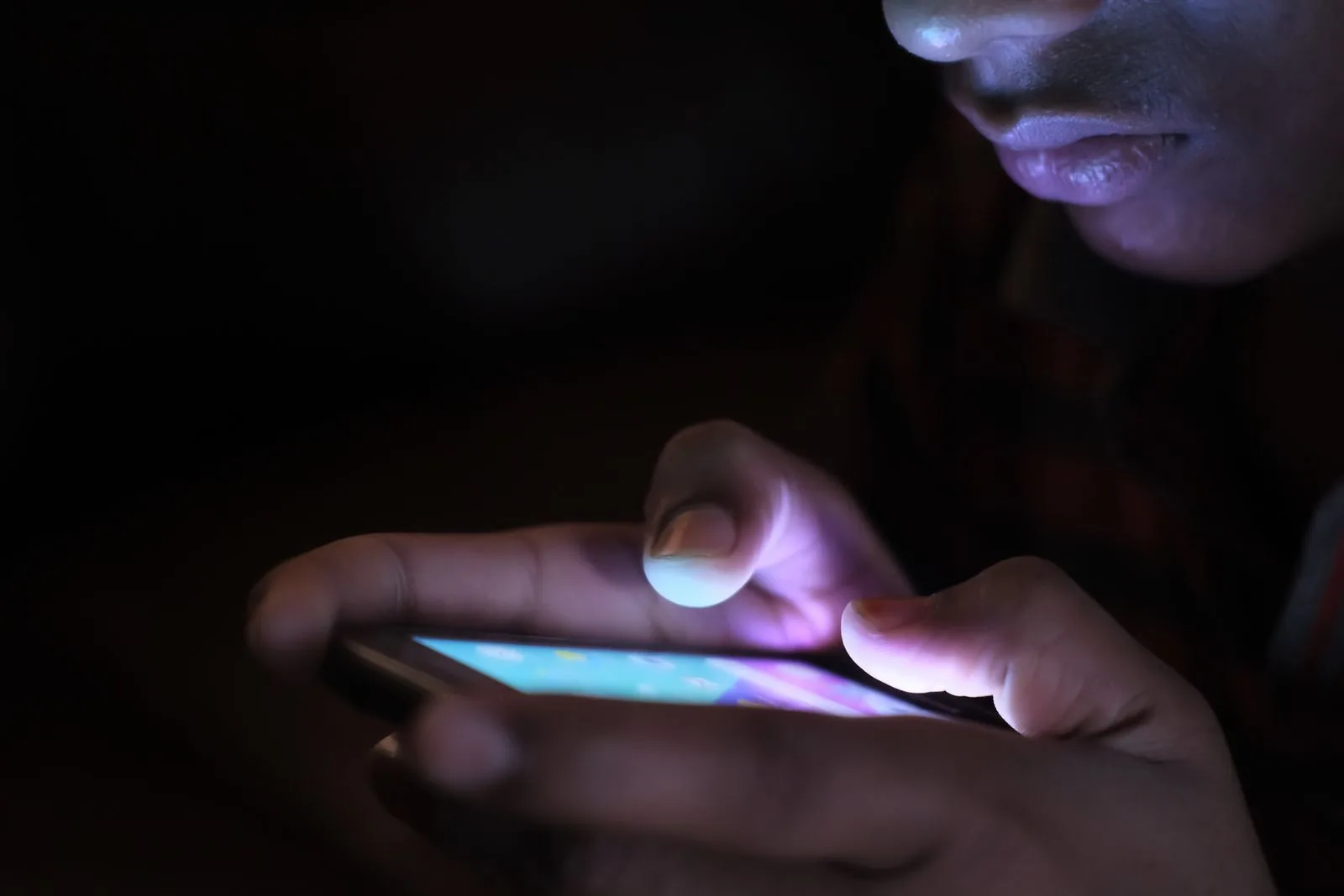 A person's hands using an illuminated smartphone in a dark room