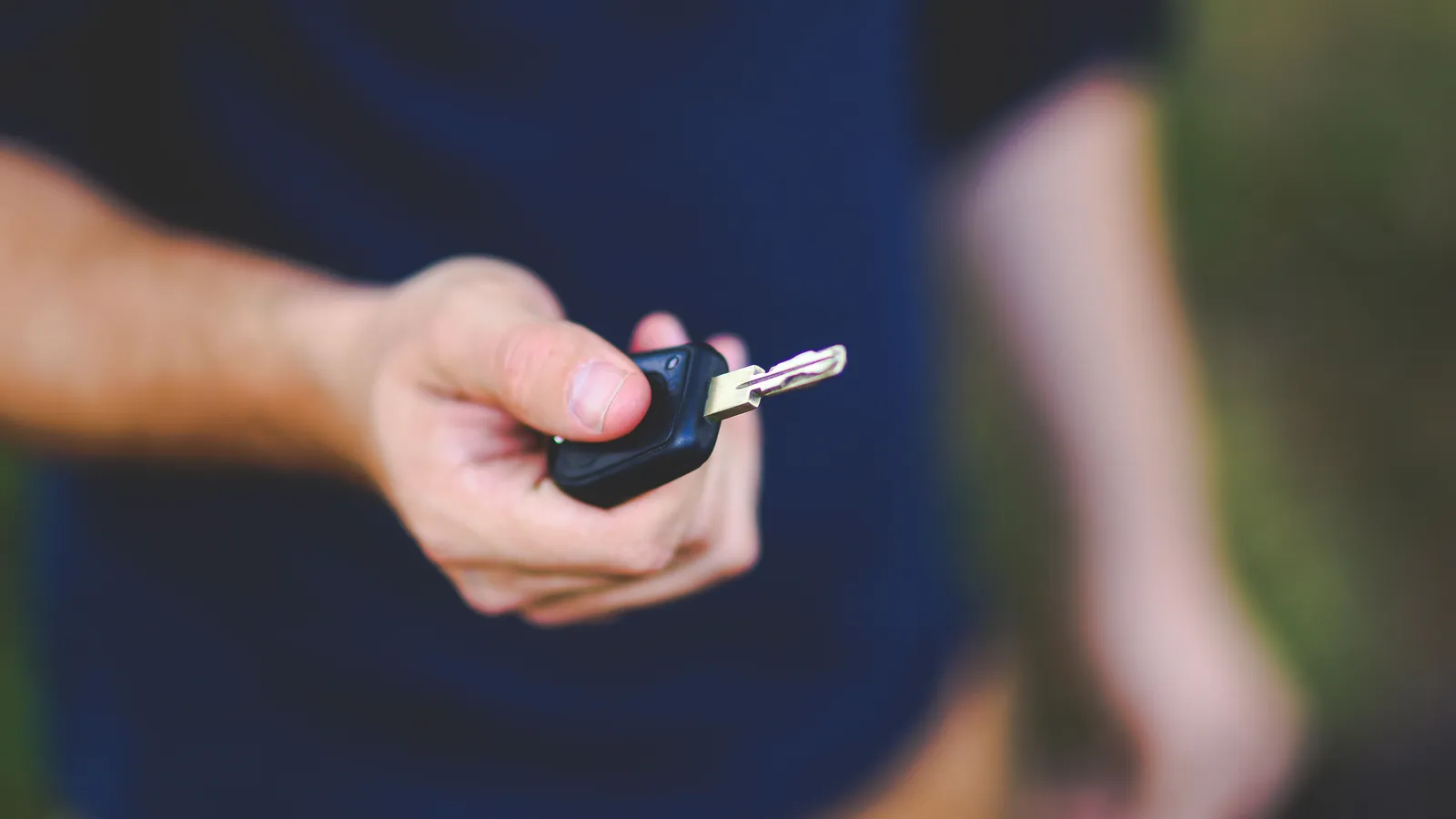 A hand holding out a black car key toward the camera