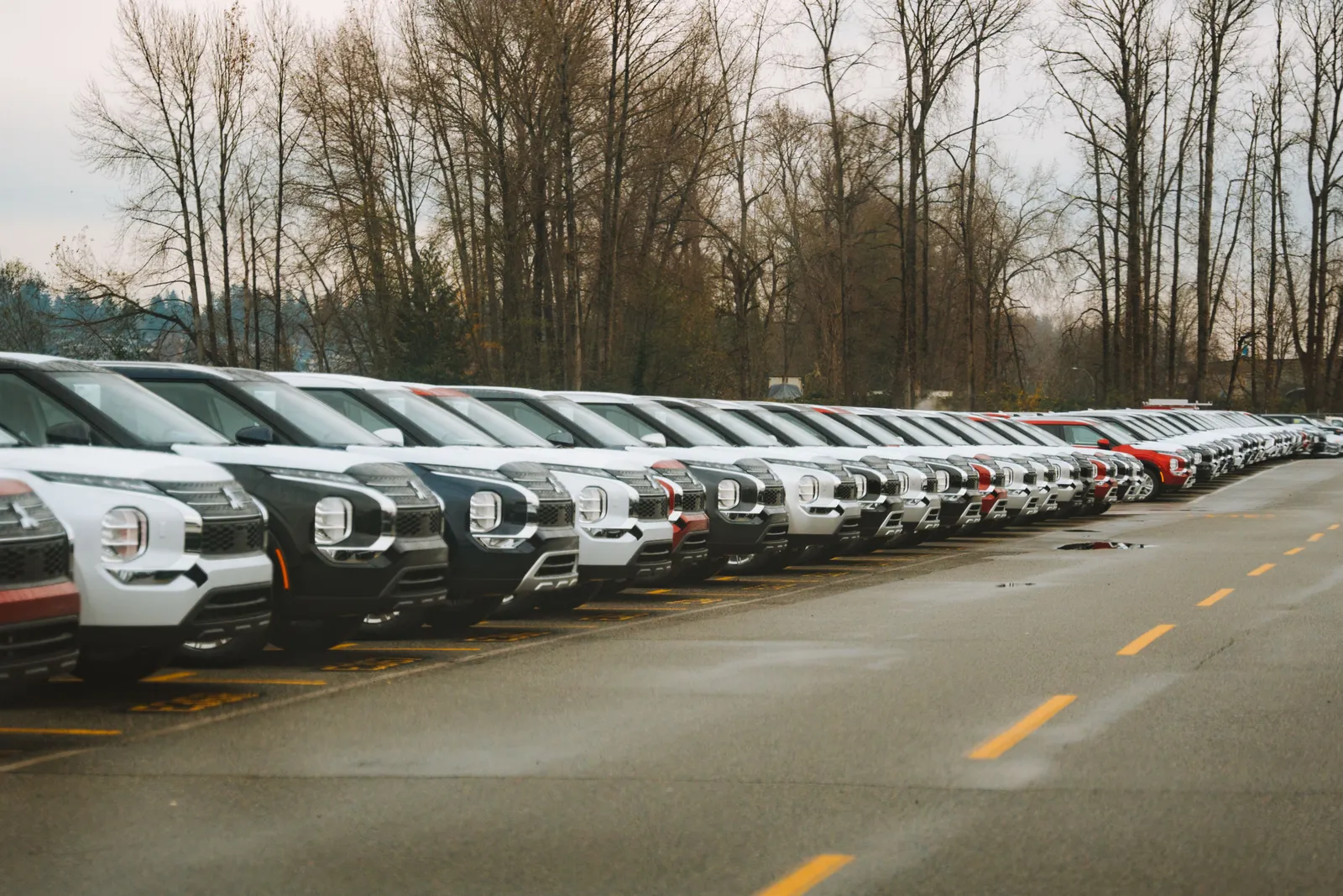 Rows of new cars parked on a dealership lot under an overcast sky
