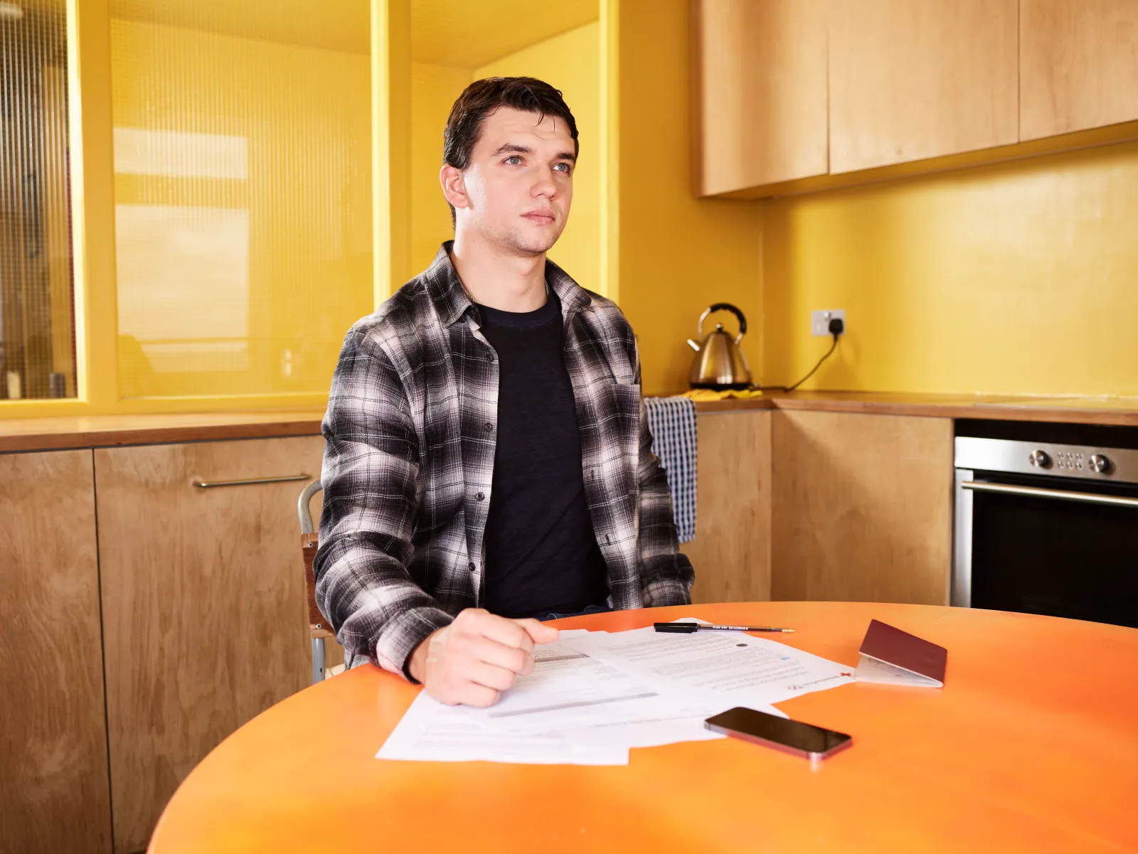 Homeowner sitting at a kitchen table reviewing a paper insurance policy under morning light
