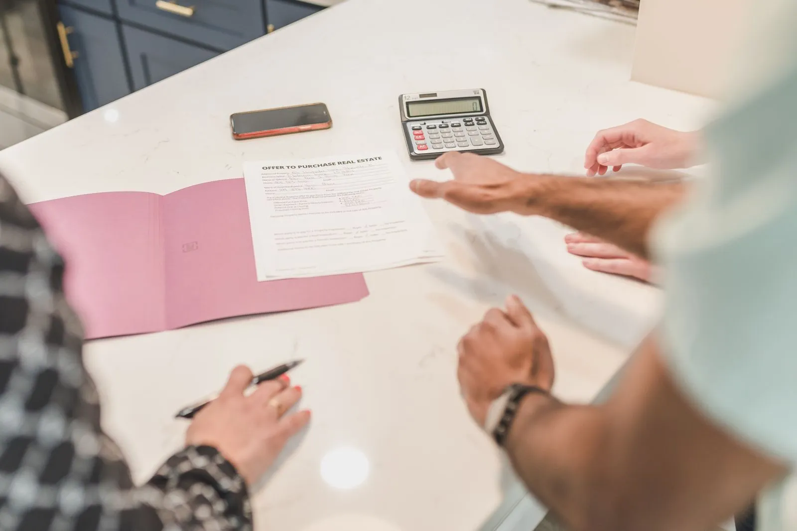 Hands gesturing across a table while reviewing a real estate document with a calculator nearby
