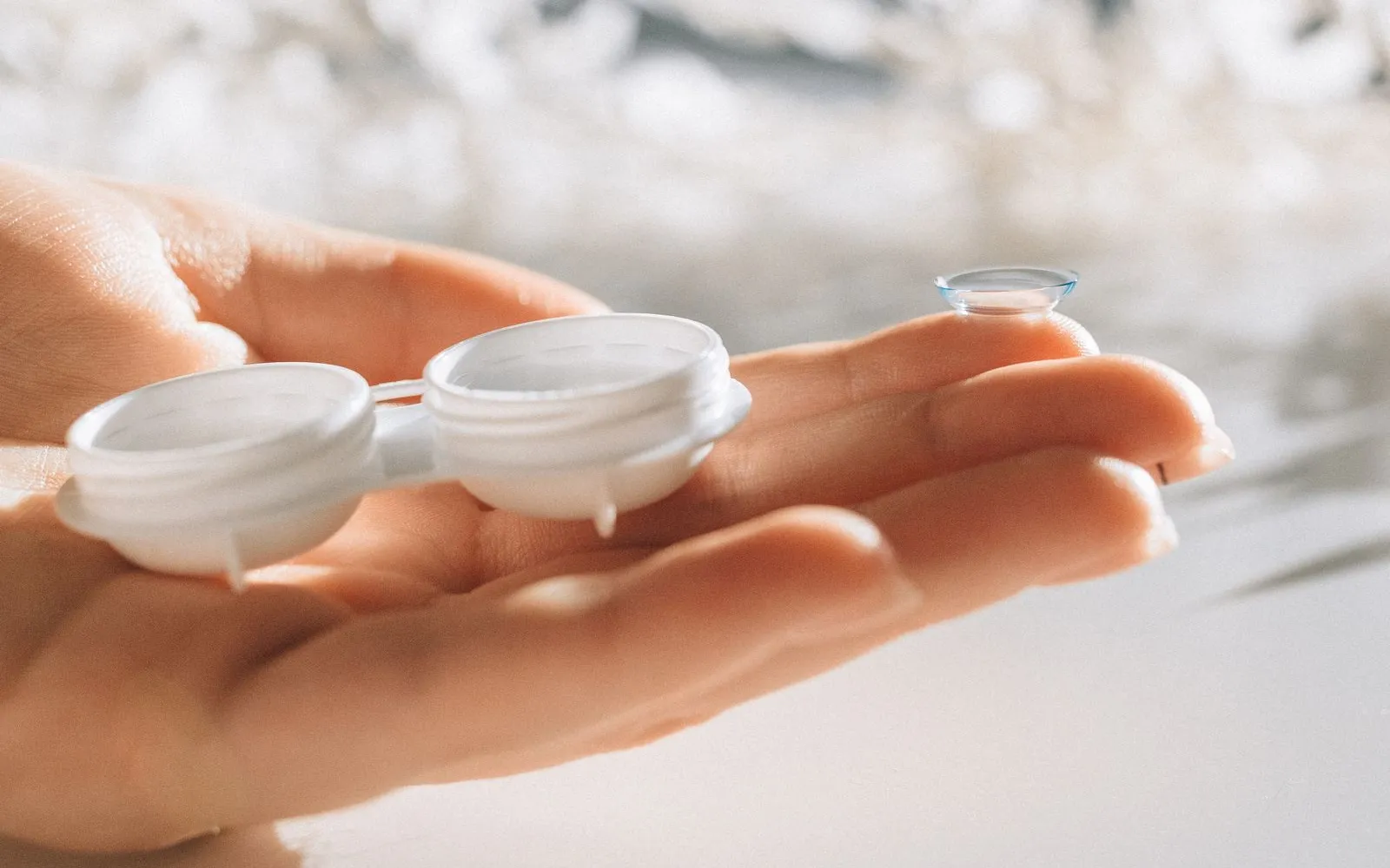 Hand holding an open contact lens case with a single lens balanced on a fingertip