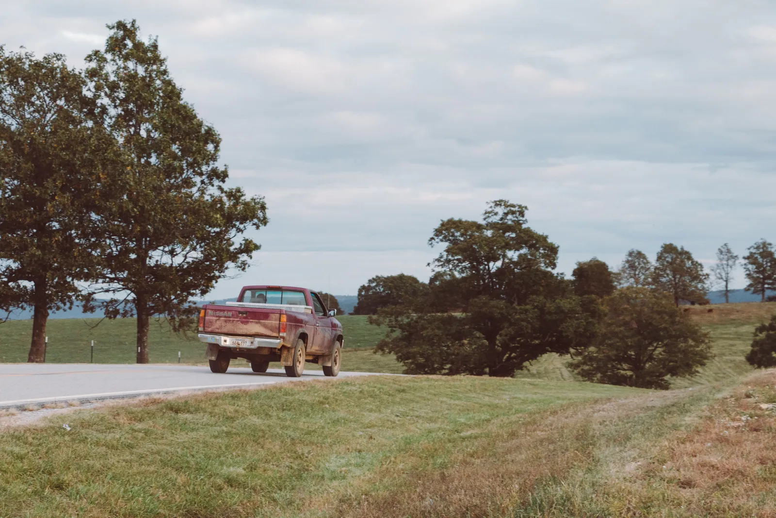 Pickup truck driving on a scenic rural road lined with green trees