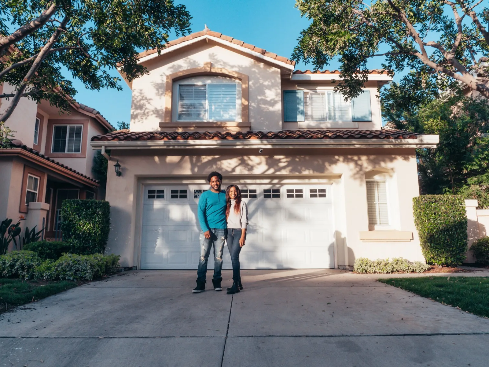A smiling couple standing outside their newly purchased house on a sunny day