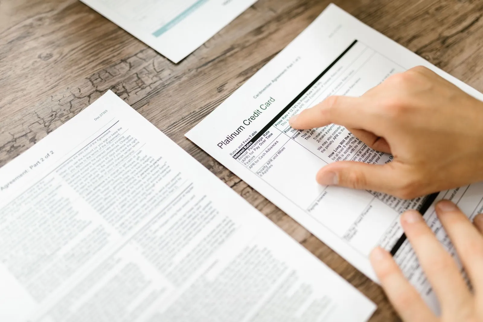 A person examining a printed credit card agreement on a wooden desk