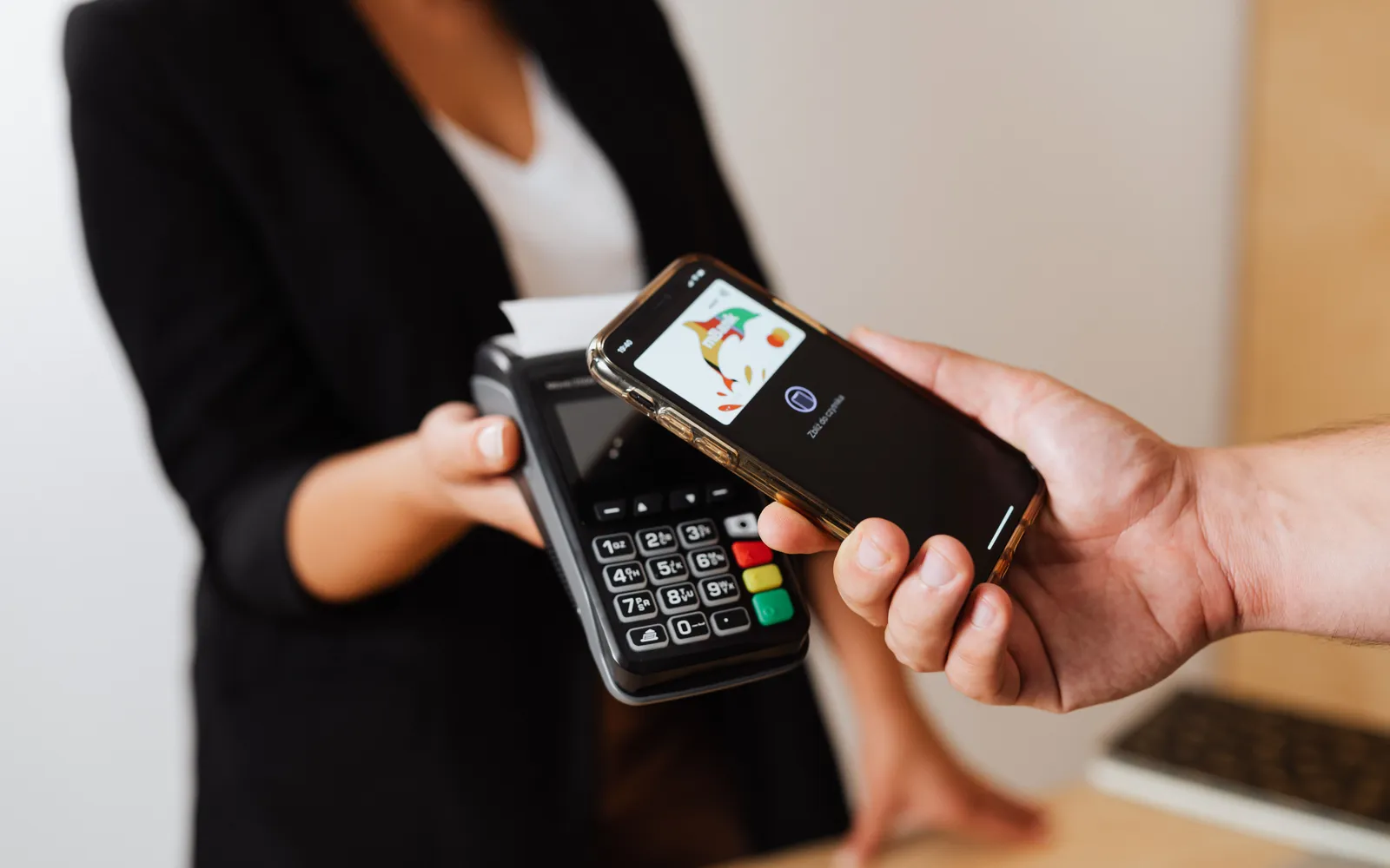 Person tapping a smartphone against a card reader at a store counter