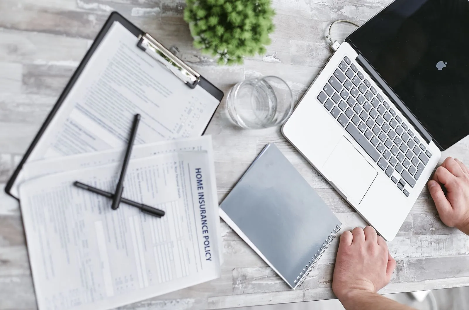 A person reviewing paperwork on a desk beside a laptop