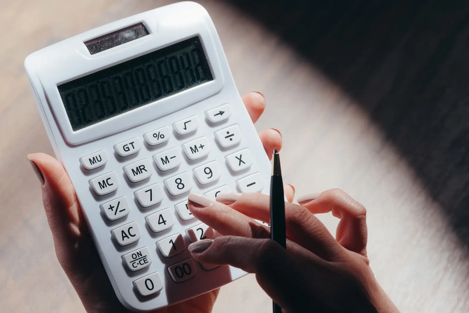 Hands holding a calculator and a pen over a wooden desk