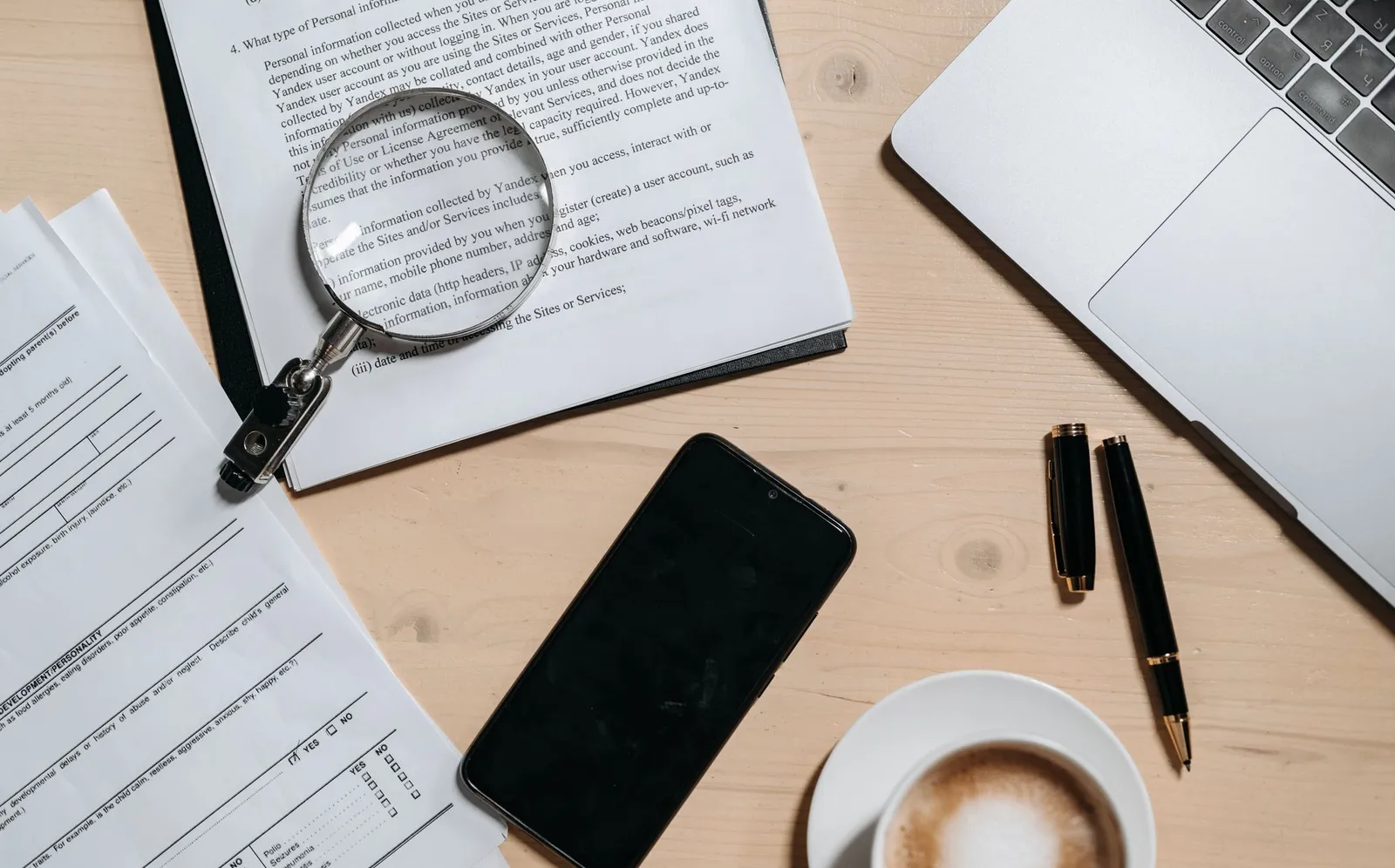Documents, a laptop, coffee and a magnifying glass on an office desk