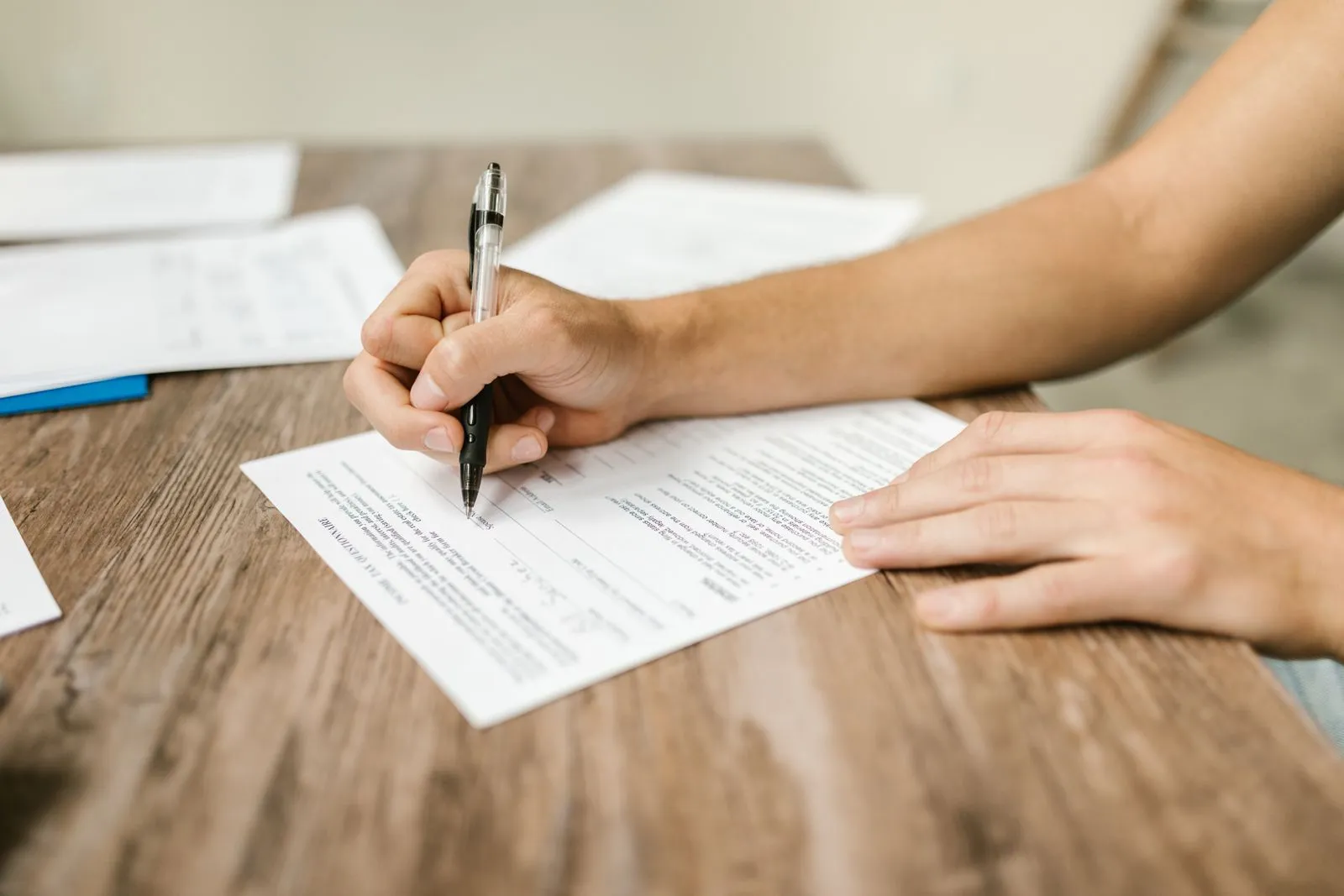 Close-up of a hand filling out paperwork with a pen on a wooden desk