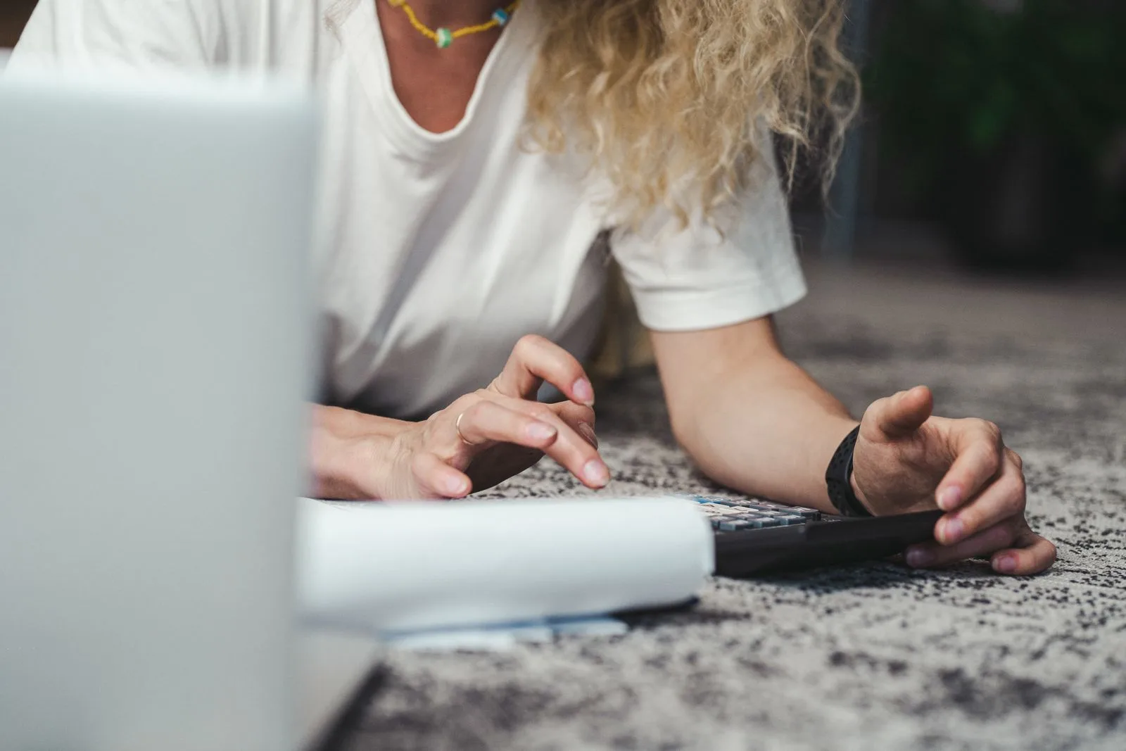 Person lying on a carpet working a desktop calculator beside a laptop and a sheet of paper