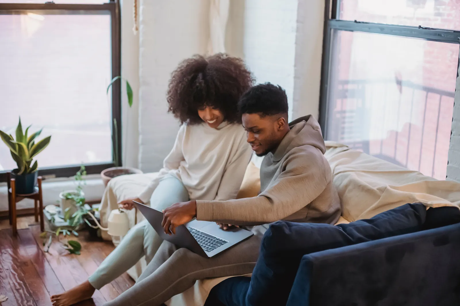 Couple sitting on a sofa looking at a laptop together in a sunlit apartment