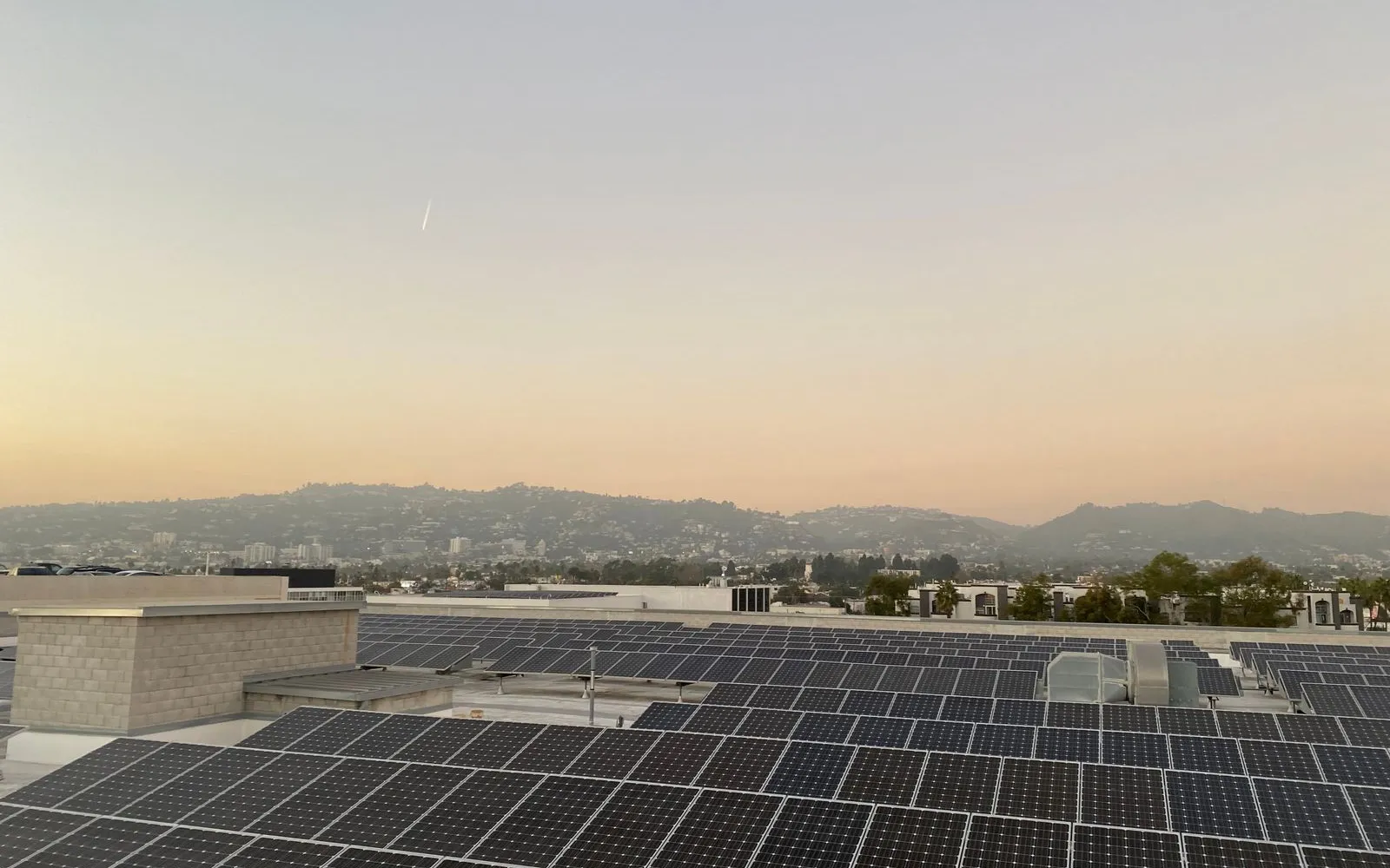 Rows of rooftop solar panels at dusk under a hazy sky, with hills in the distance