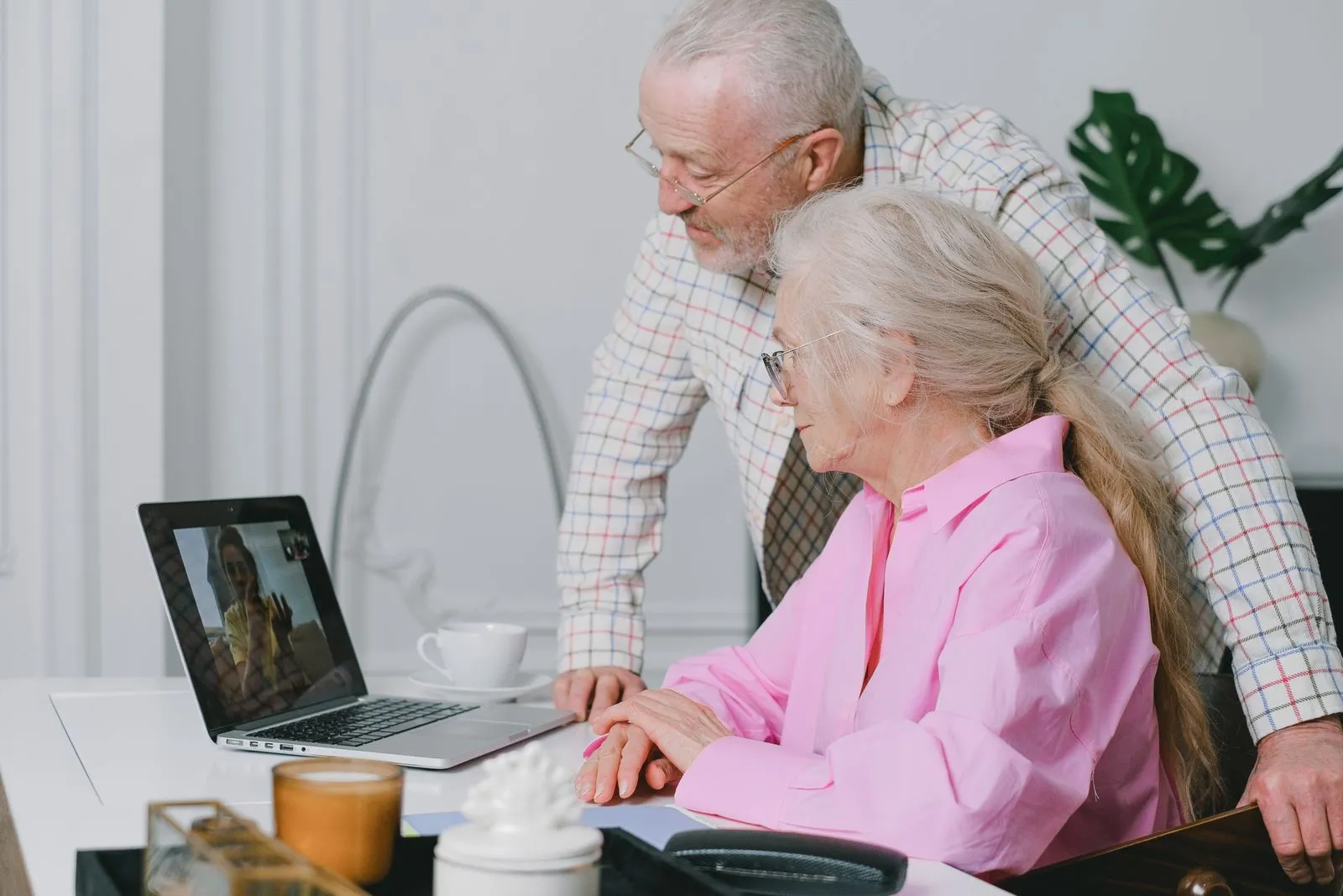Retired couple reviewing paperwork at a kitchen table with a laptop