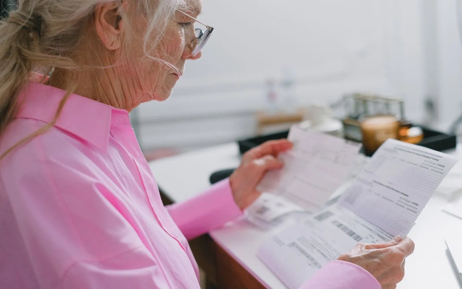 Older person at a kitchen table reviewing paperwork and a bank statement with a calculator