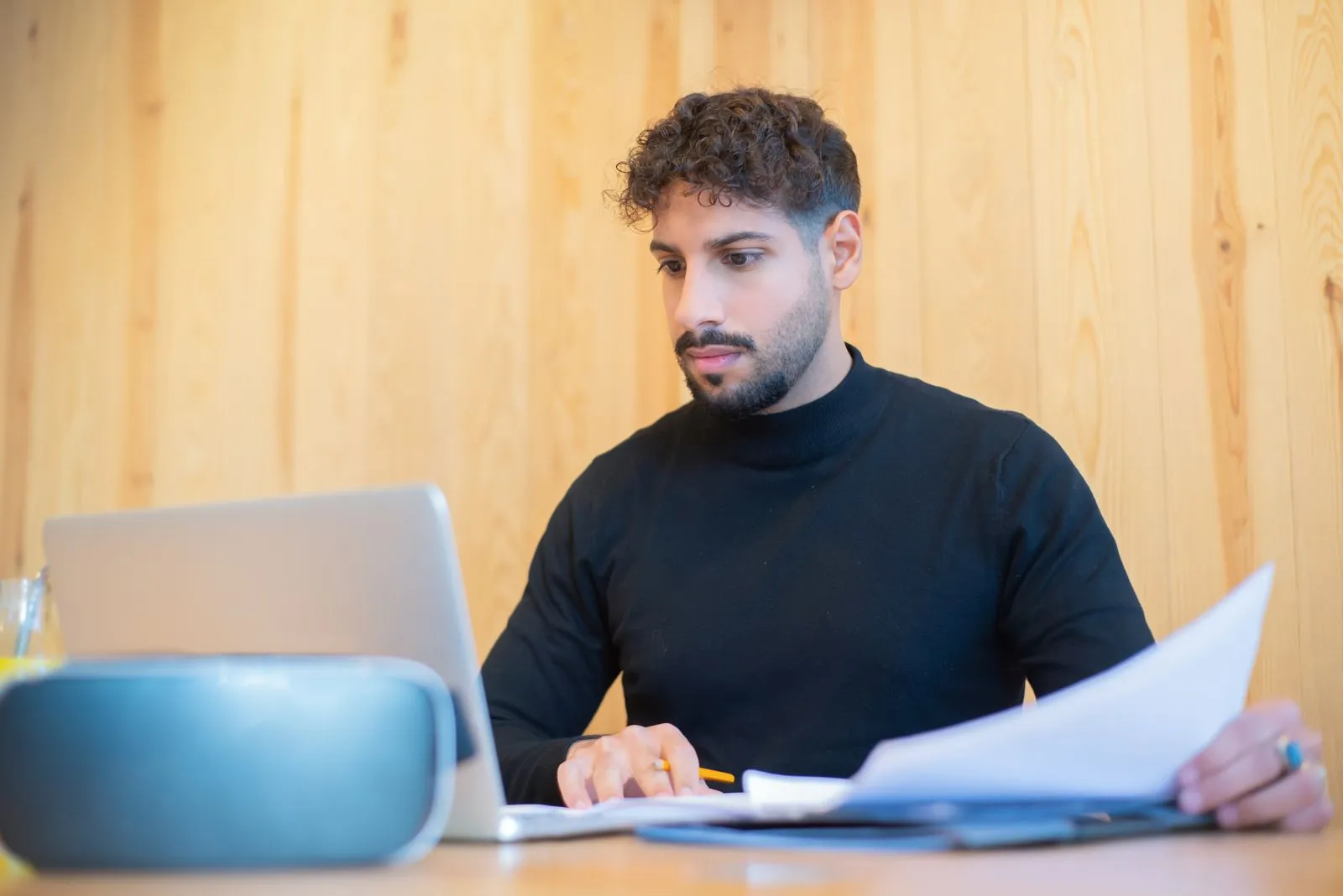 Young professional reviewing benefits paperwork at a home desk with a laptop open