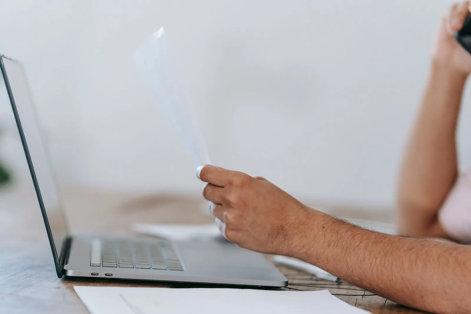 A person reading a document while holding a phone at a home desk