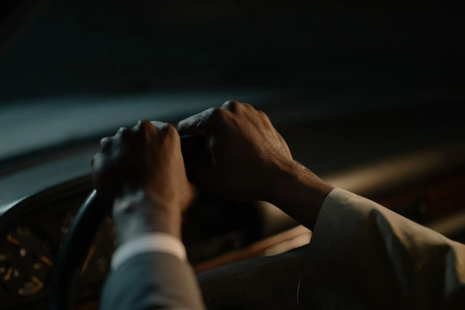 A driver's hands on the steering wheel in a dimly lit car interior at night