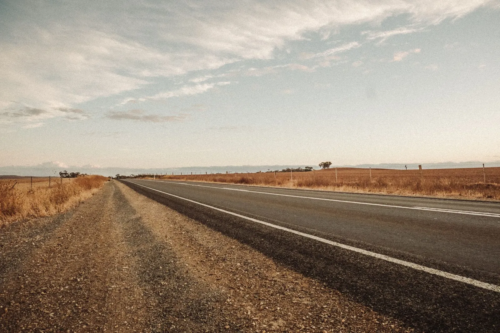 An empty two-lane highway running through dry golden fields under a wide open sky