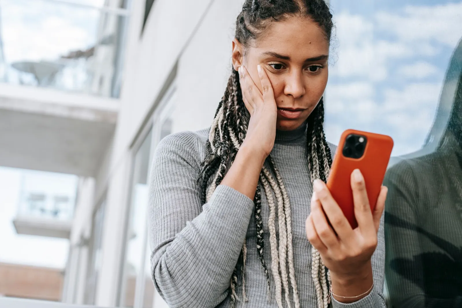 Woman on a city sidewalk checking a bank alert on her smartphone with a concerned expression