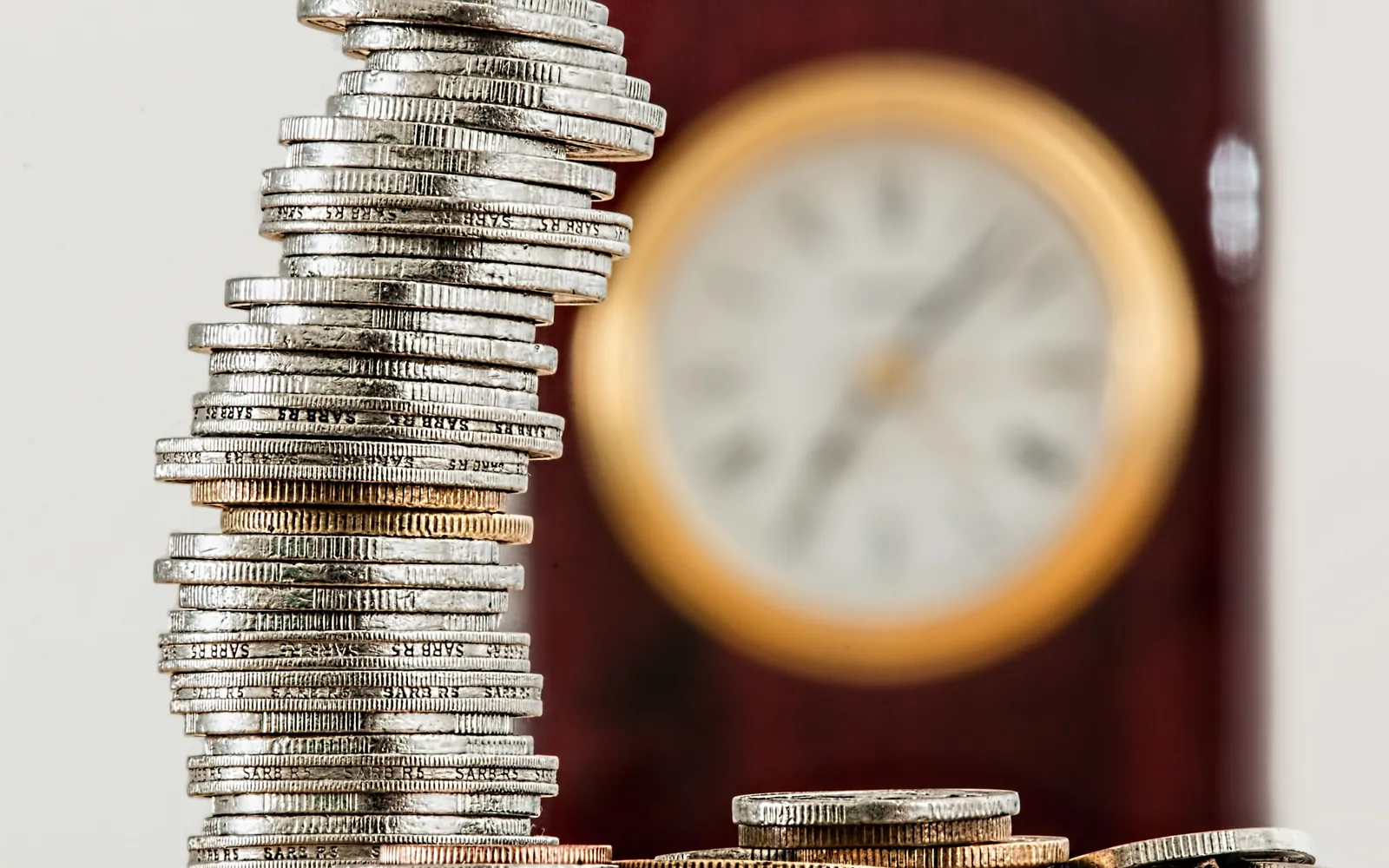 Stacked coins beside a small clock